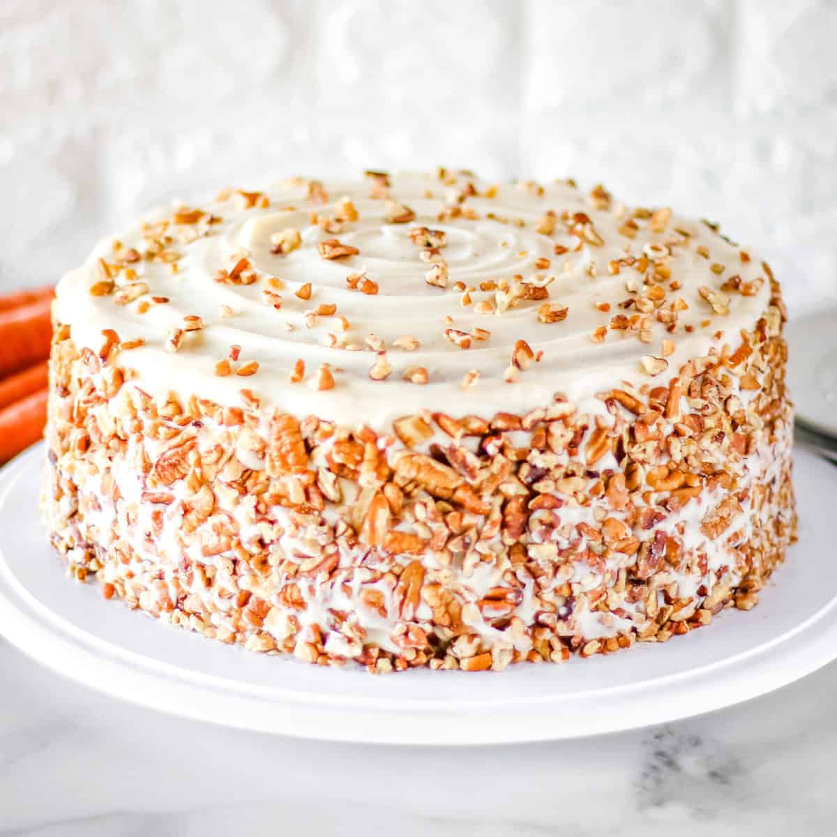 Homemade carrot cake with cream cheese frosting on a white cake platter.