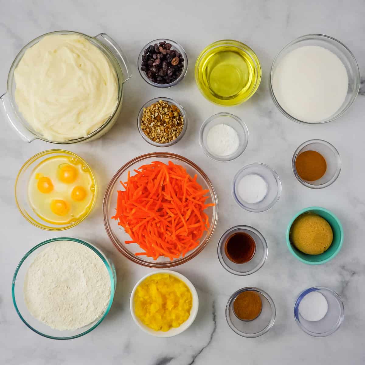 All the simple ingredients used to make homemade carrot cake on a marble counter top.