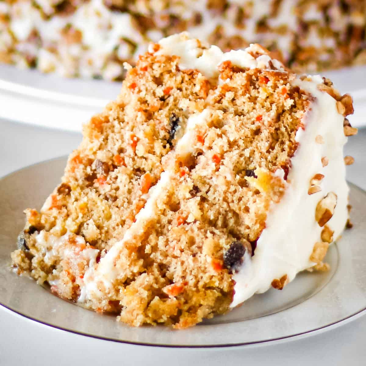 A slice of homemade carrot cake with cream cheese frosting on a white plate.