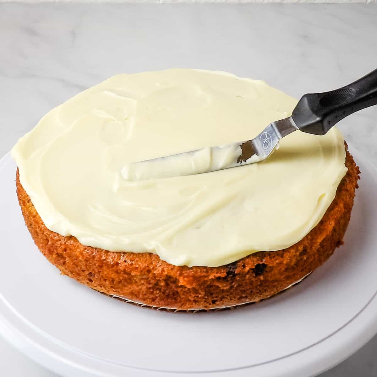 Icing homemade carrot cake with cream cheese frosting using an icing spatula.