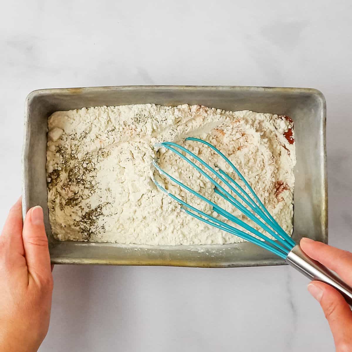Mixing seasoned flour together in a baking pan.