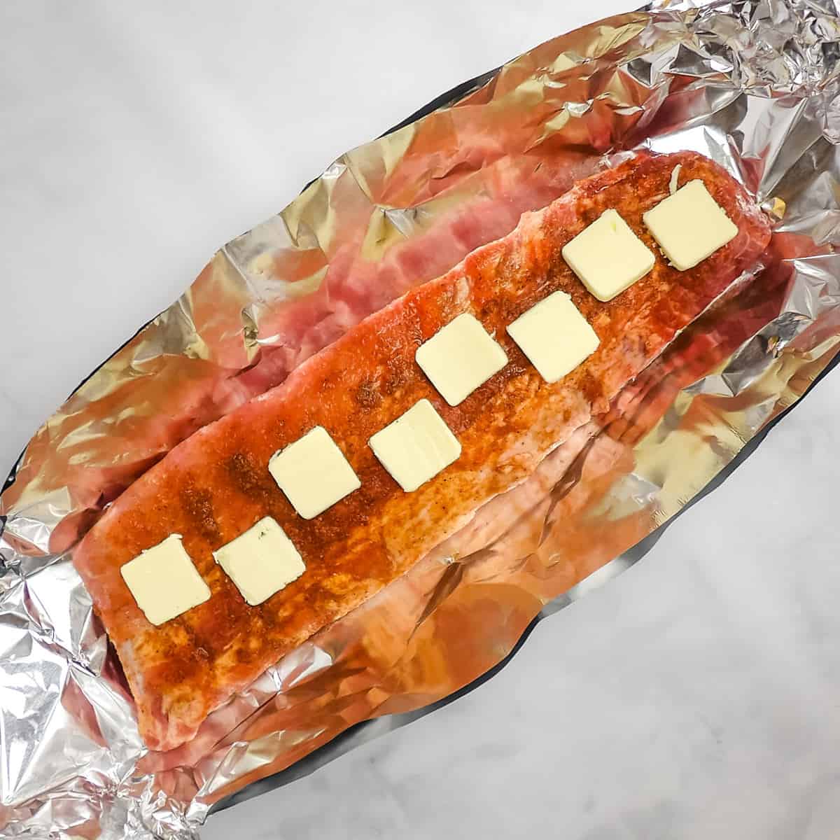 Baby back ribs in a foil boat with braising liquid ingredients on top.