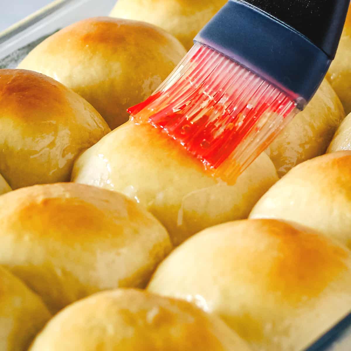 Brushing the tops of the bread rolls with melted butter.