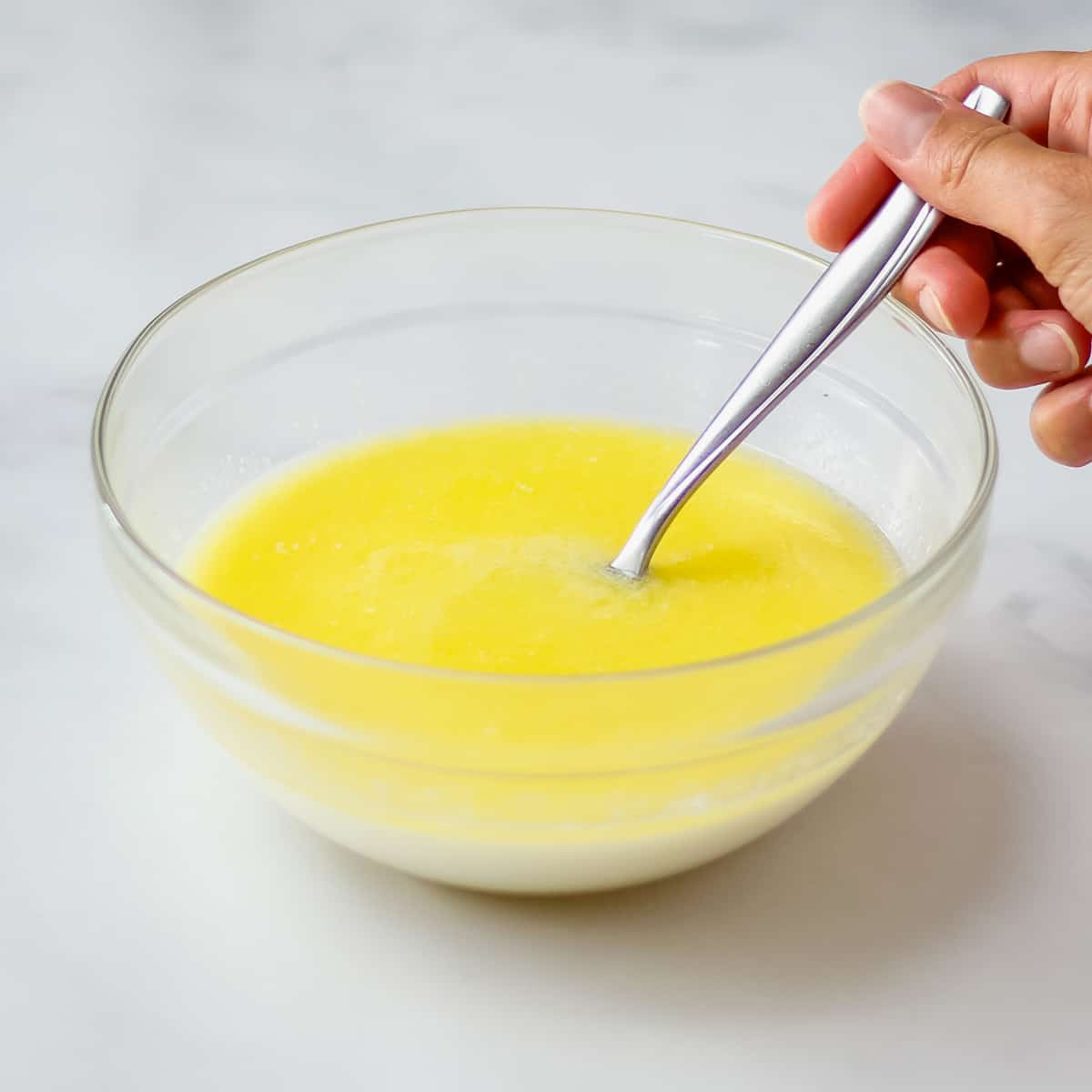 Stirring milk, sugar, and melted butter together in a glass bowl.