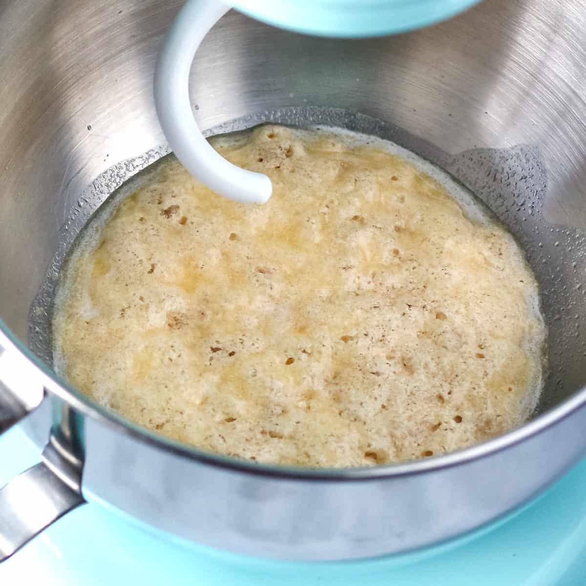Foamy activated yeast mixture in the metal mixing bowl of a blue stand mixer.
