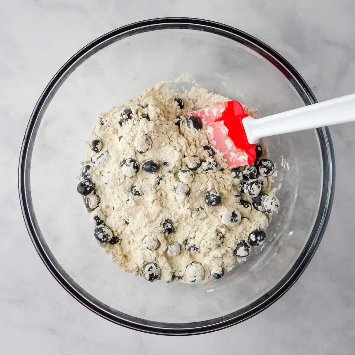 Tossing blueberries in the flour mixture with a red and white spatula.