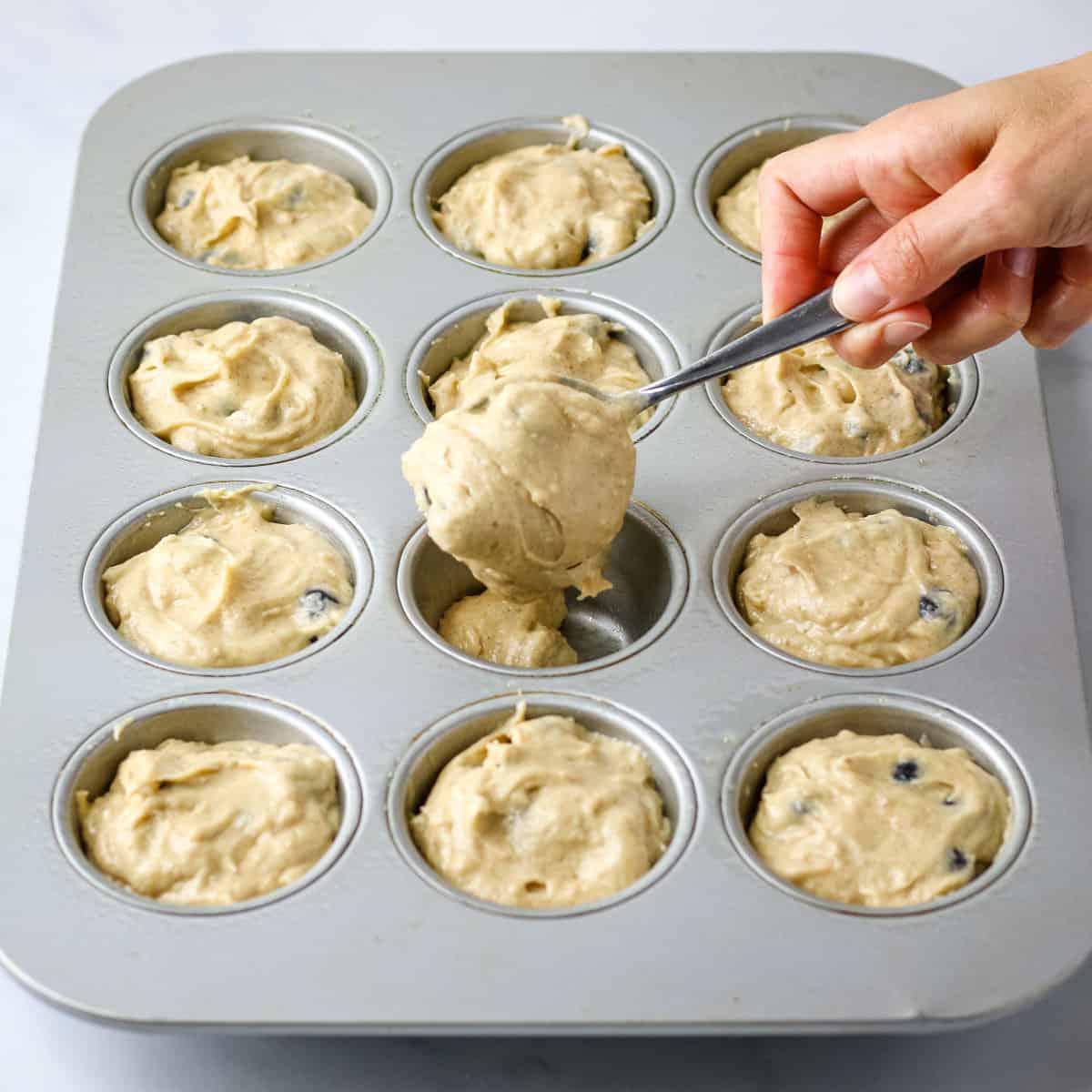 Spooning muffin batter into a greased muffin pan.