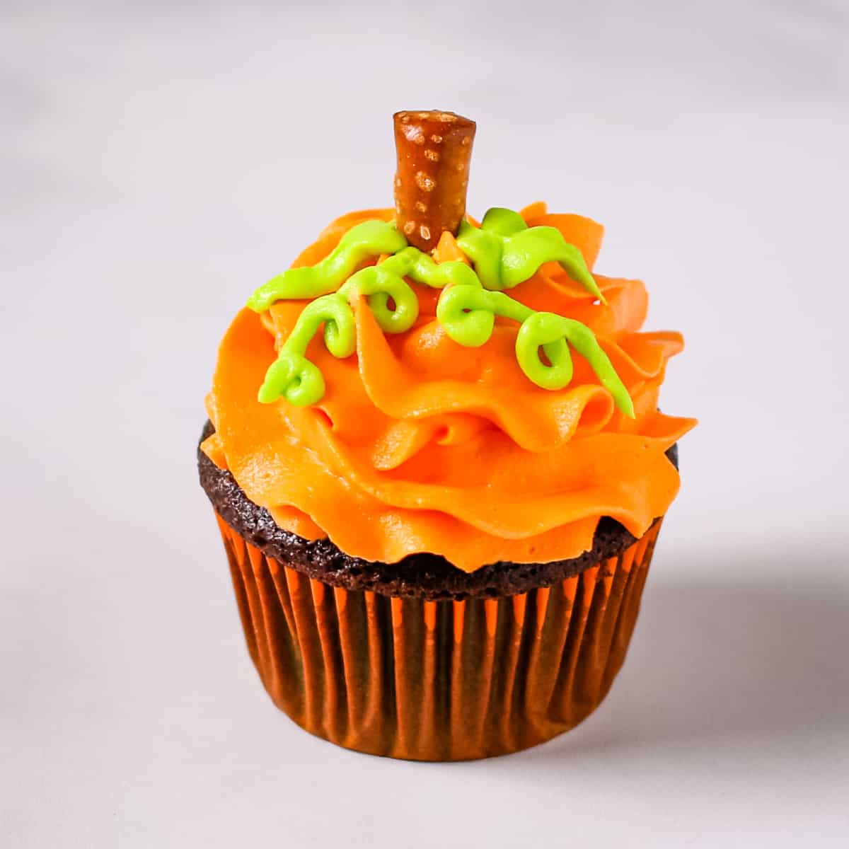 A chocolate cupcake decorated as an orange Halloween pumpkin.