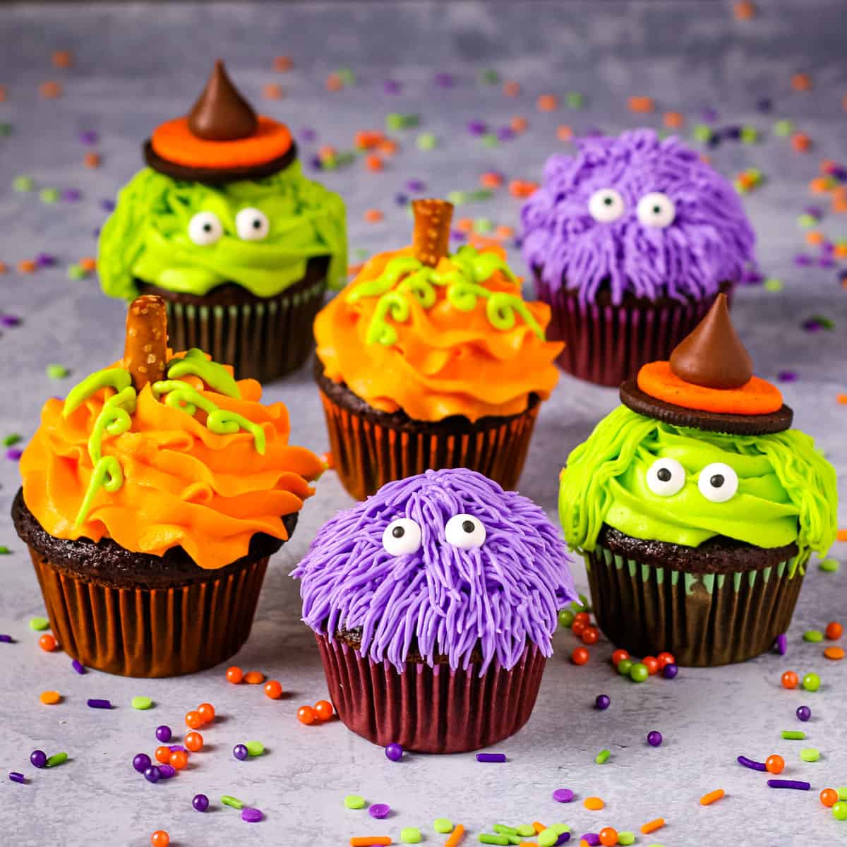 Cute Halloween cupcakes decorated as purple monsters, green witches, and orange pumpkins.