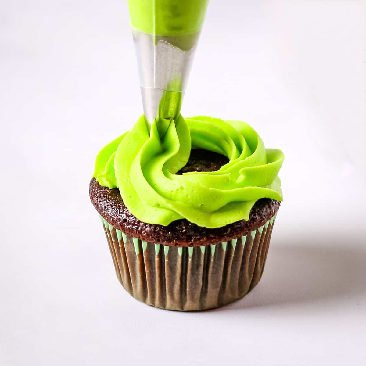 Piping a green buttercream swirl on top of a chocolate cupcake.