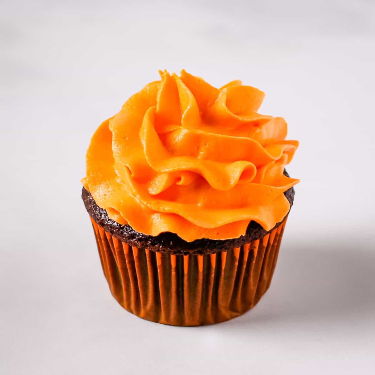 Orange buttercream swirl on top of a chocolate cupcake.