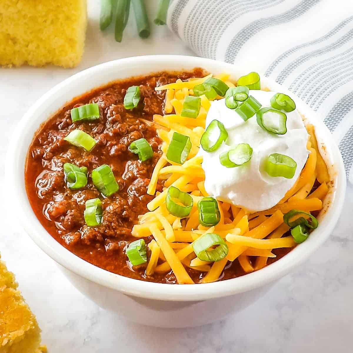 Slow cooker venison chili (deer chili) topped with cheese, sour cream, and green onions in a white bowl.