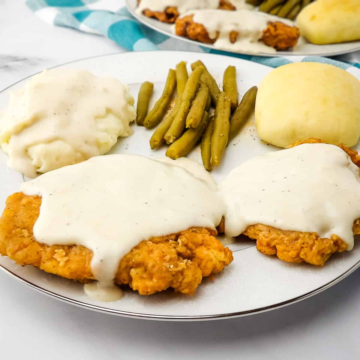 Chicken Fried Elk Steak topped with white cream gravy on a white plate.