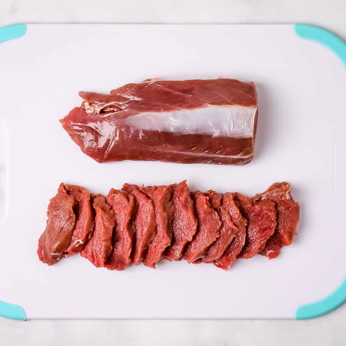 Deer backstrap cut into thin slices on a white cutting board.