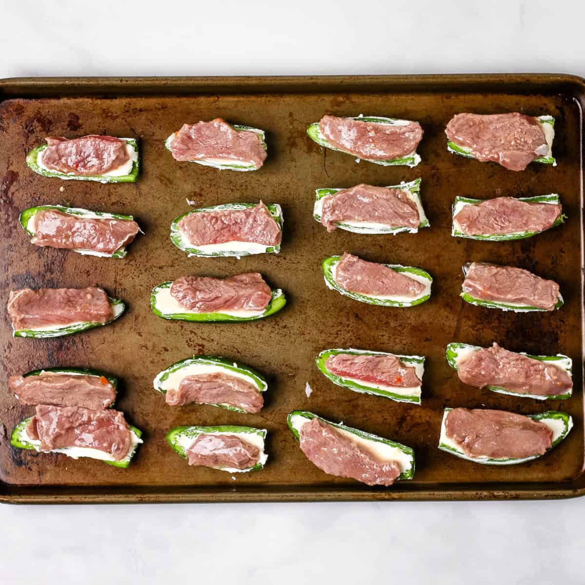 Sliced deer backstrap laying on halved jalapeno peppers stuffed with cream cheese.