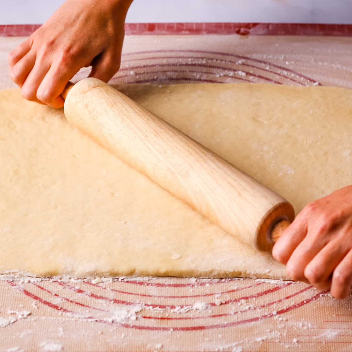 Rolling the dough into a rectangle with a wooden rolling pin.