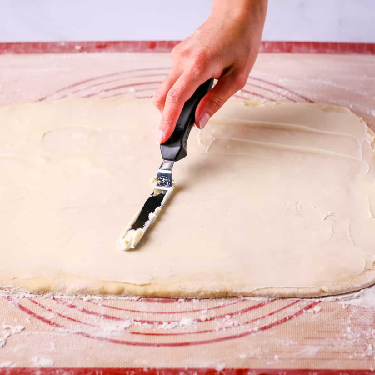 Spreading butter on top of the dough with a small metal spatula.
