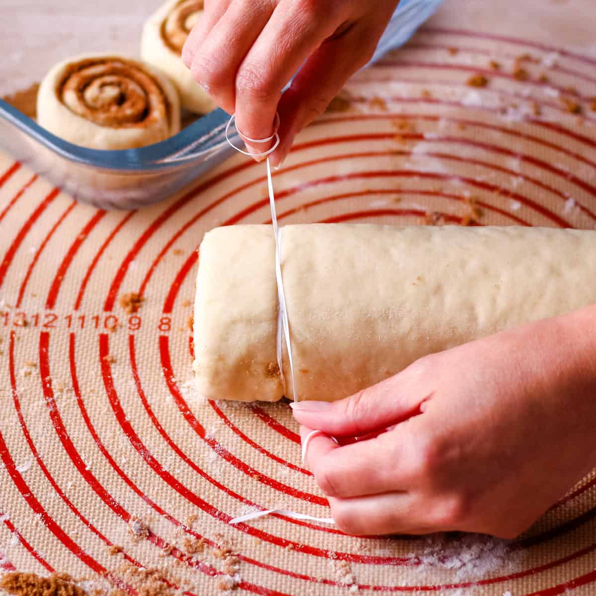 Cutting the cinnamon roll dough log with a piece of dental floss.