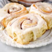 Homemade cinnamon rolls topped with cream cheese frosting on a white plate.