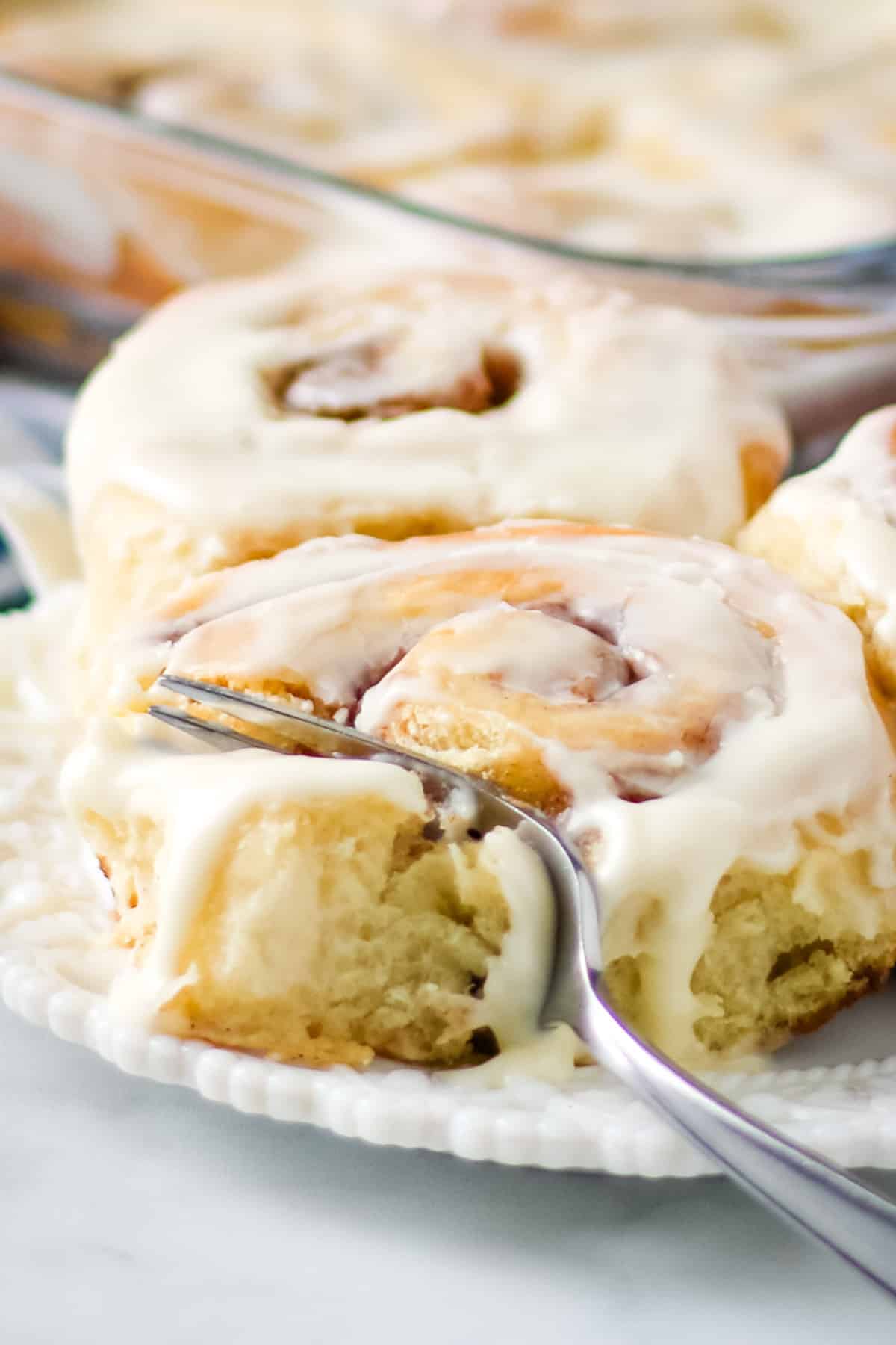 Cutting into a homemade cinnamon roll topped with cream cheese frosting with a silver fork.