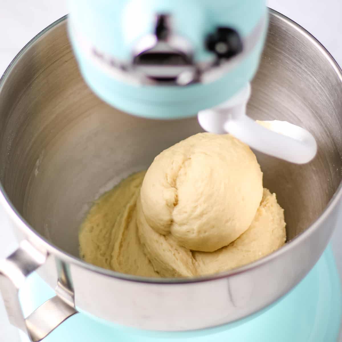 Cinnamon roll dough in the mixing bowl of a blue stand mixer.