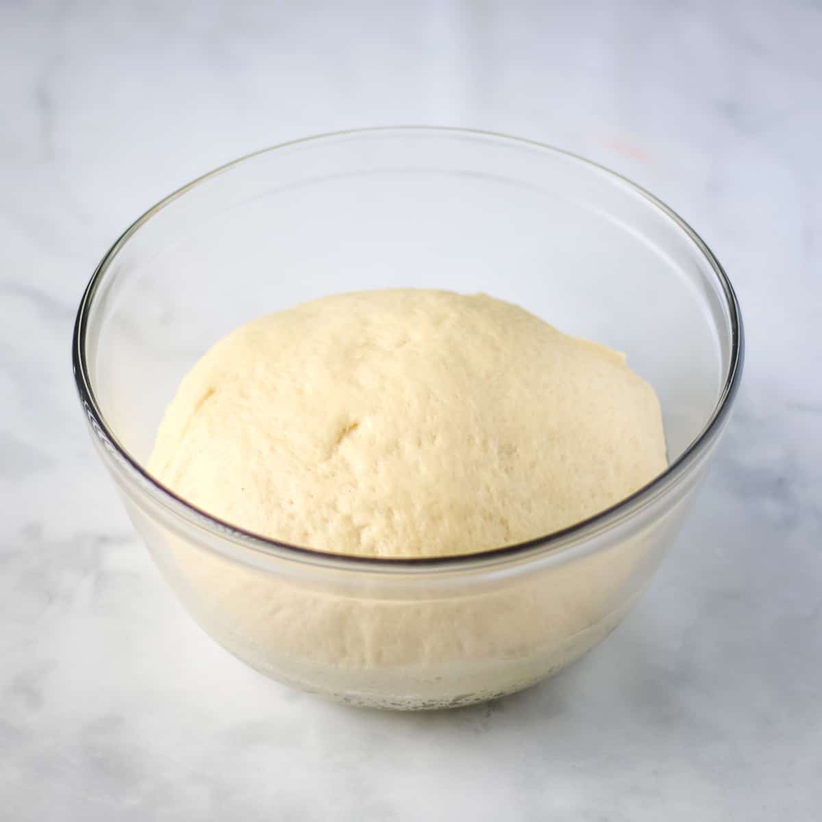 Risen dough in a clear glass bowl.