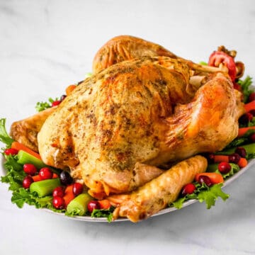 Baked turkey on a white serving platter decorated with lettuce, celery, carrots, and cranberries.