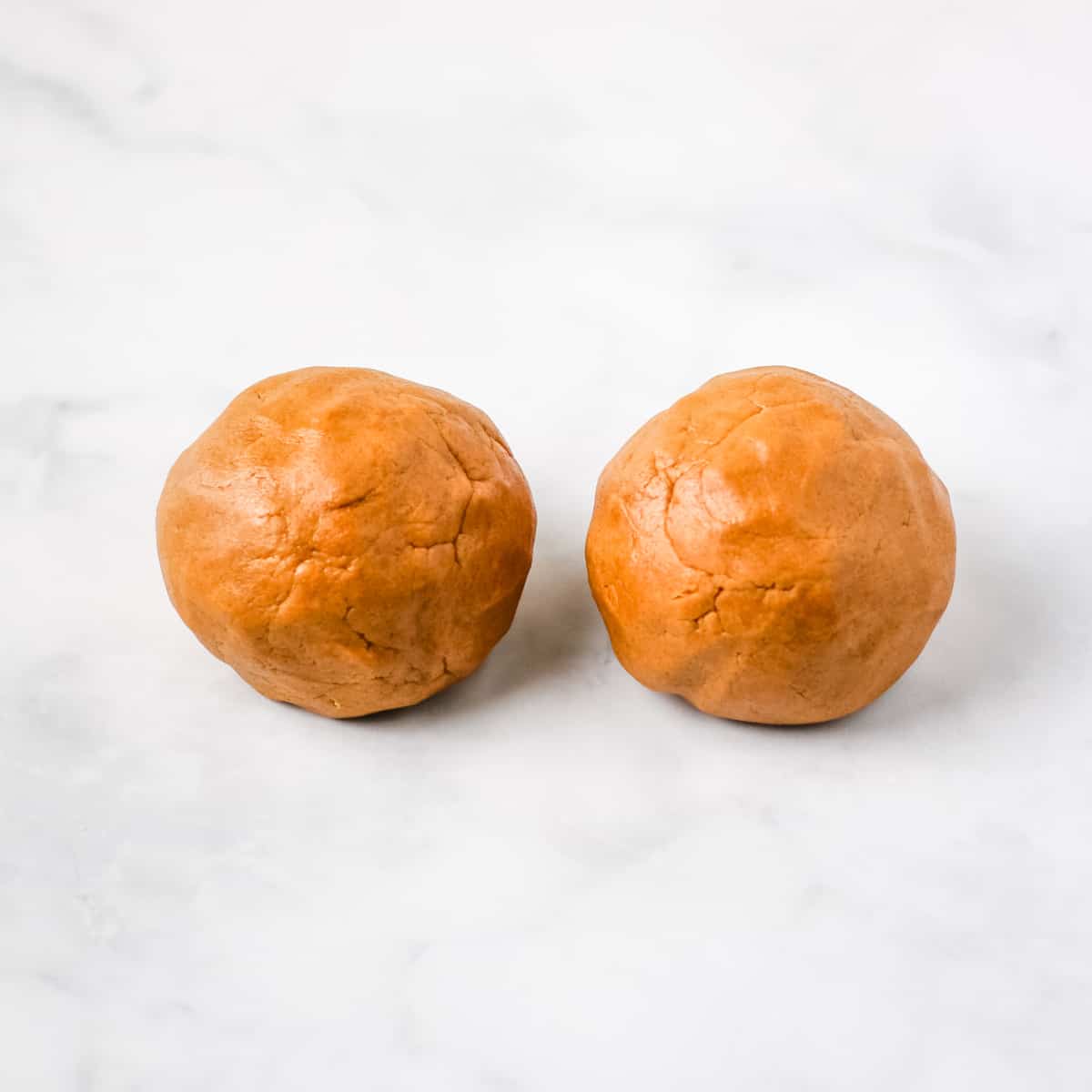 Two equal sized cookie dough balls on a marble countertop.