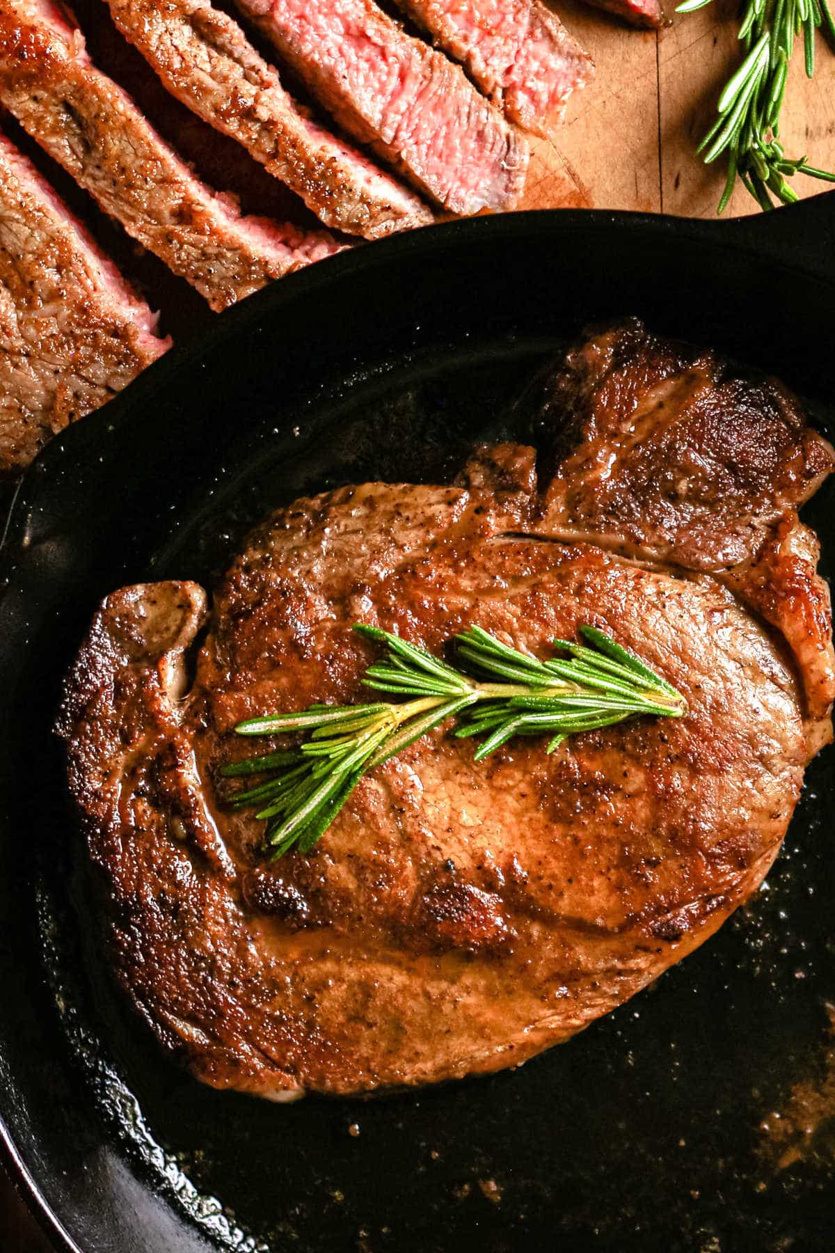 Pan seared steak in a cast iron skillet garnished with fresh rosemary.