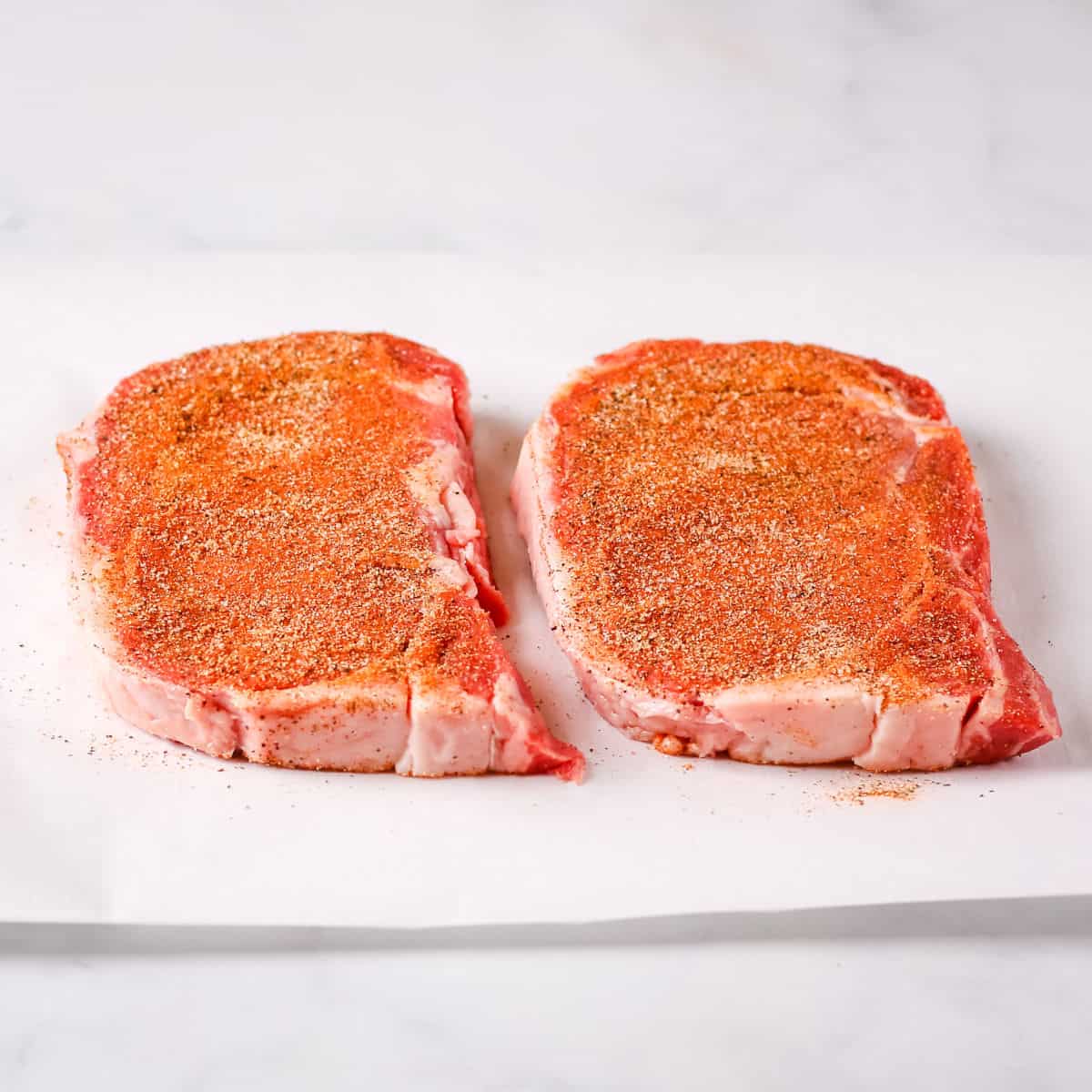 Seasoned ribeye steaks on a white plate lined with paper towels.