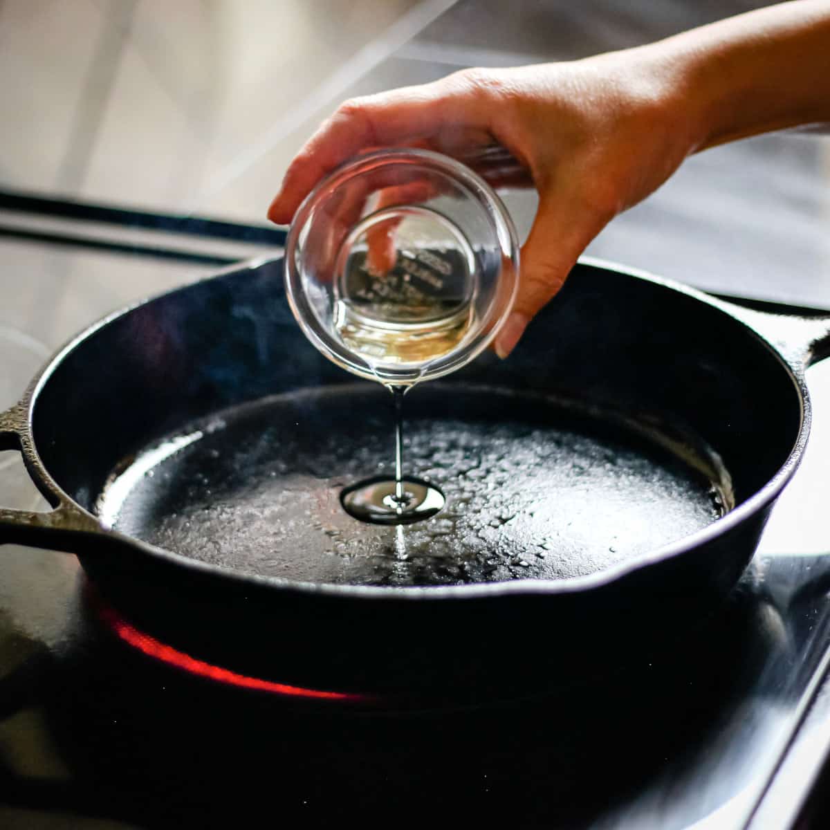 Pouring cooking oil into a large cast iron skillet.