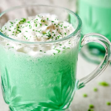 Green shamrock shake garnished with whipped cream and green sanding sugar in a glass cup.