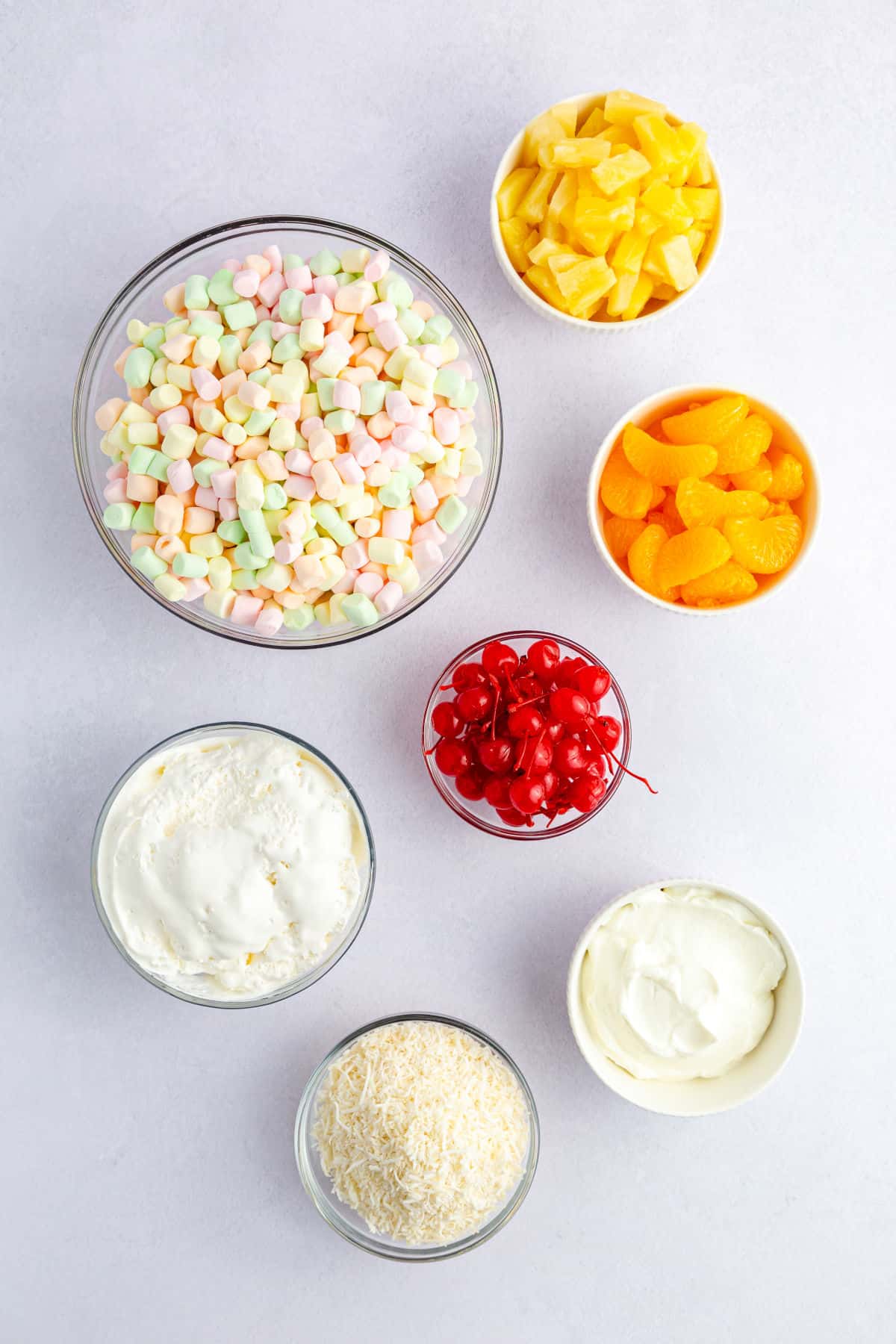 Ambrosia salad ingredients: sour cream, cool whip, marshmallows, oranges, pineapples, and cherries.
