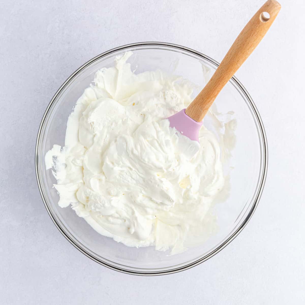 Stirring the sour cream and cool whip together in a glass bowl with a wooden spoon.