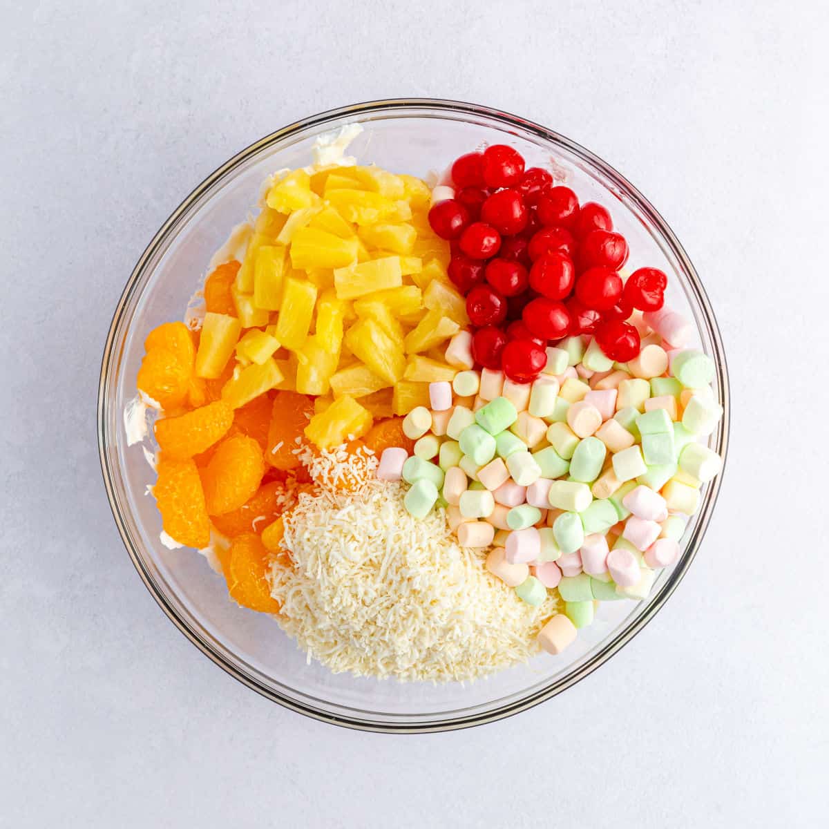 All the ambrosia salad ingredients added to a glass bowl.