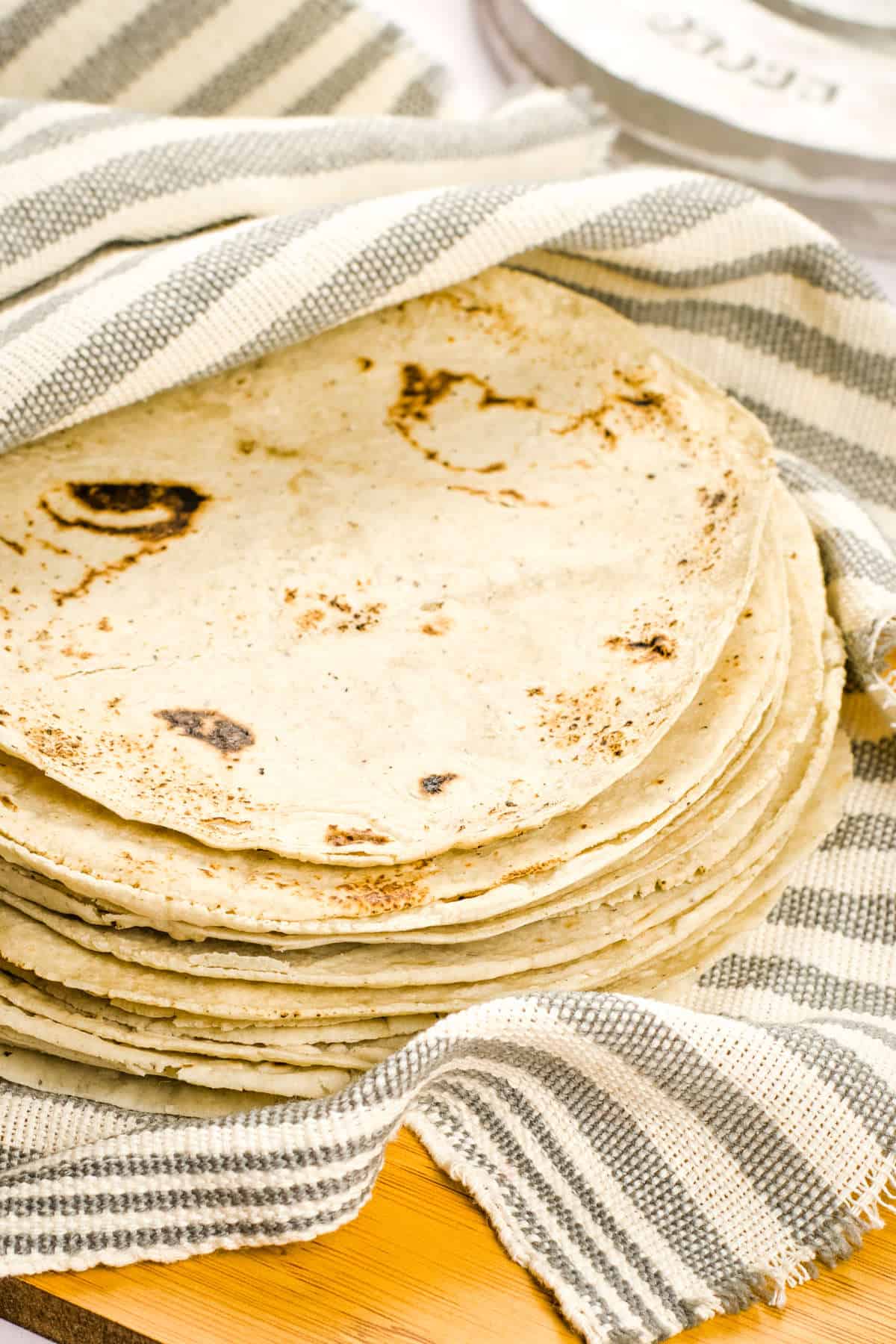 Stacked homemade tortillas partially wrapped in a grey and white striped cloth.