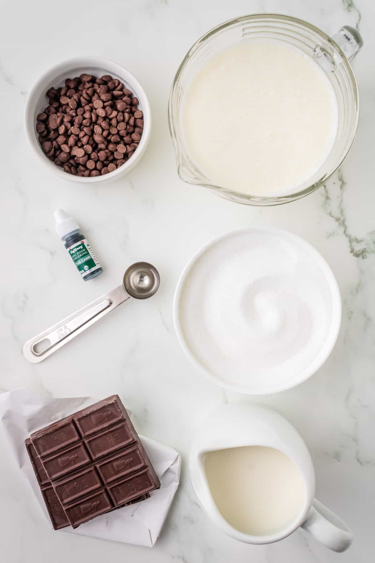 Ingredients for mint chip ice cream: heavy cream, sugar, milk, chocolate candy bar, chocolate chips, mint extract, and green food coloring.