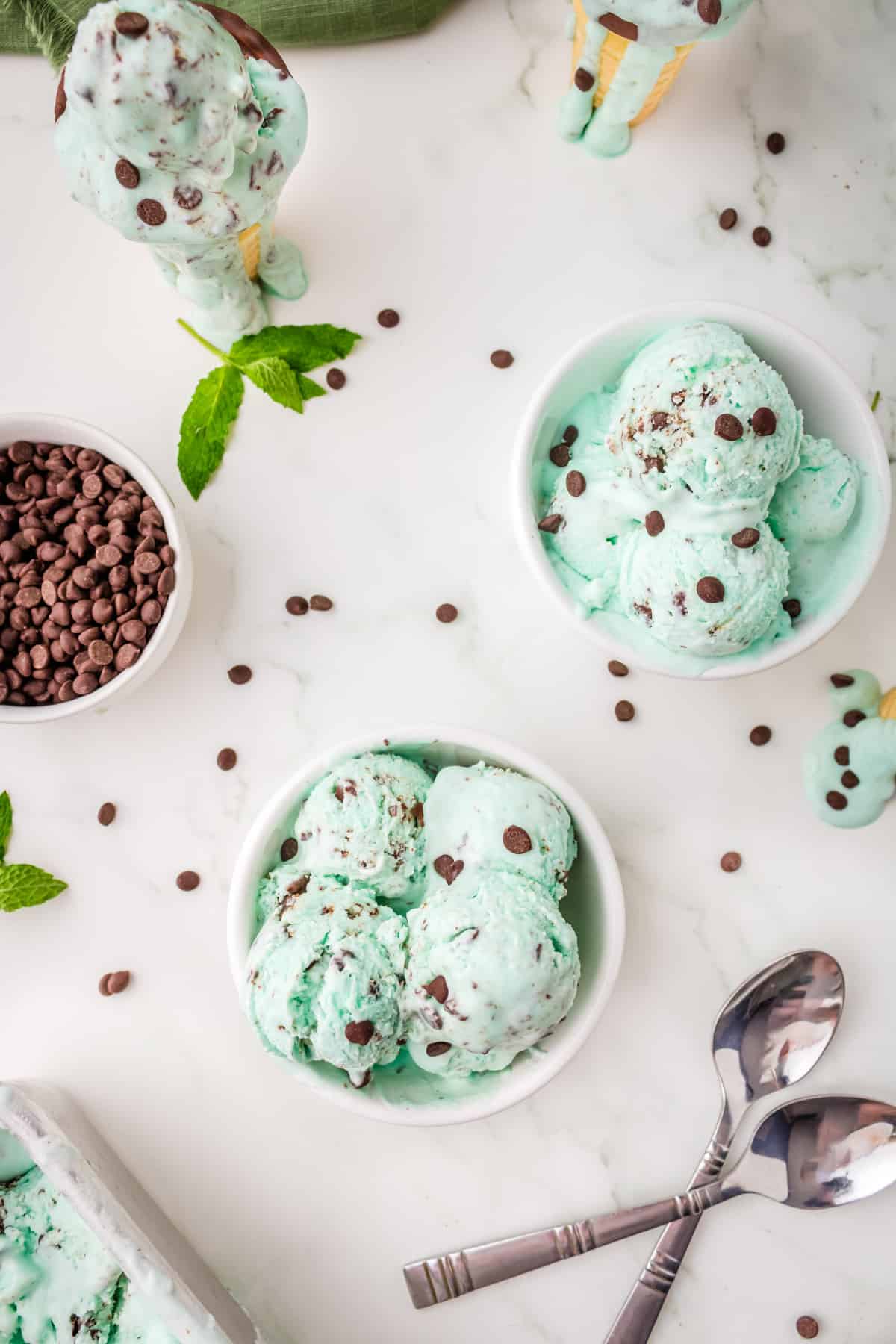 Green homemade ice cream in white bowls with chocolate chips on top.