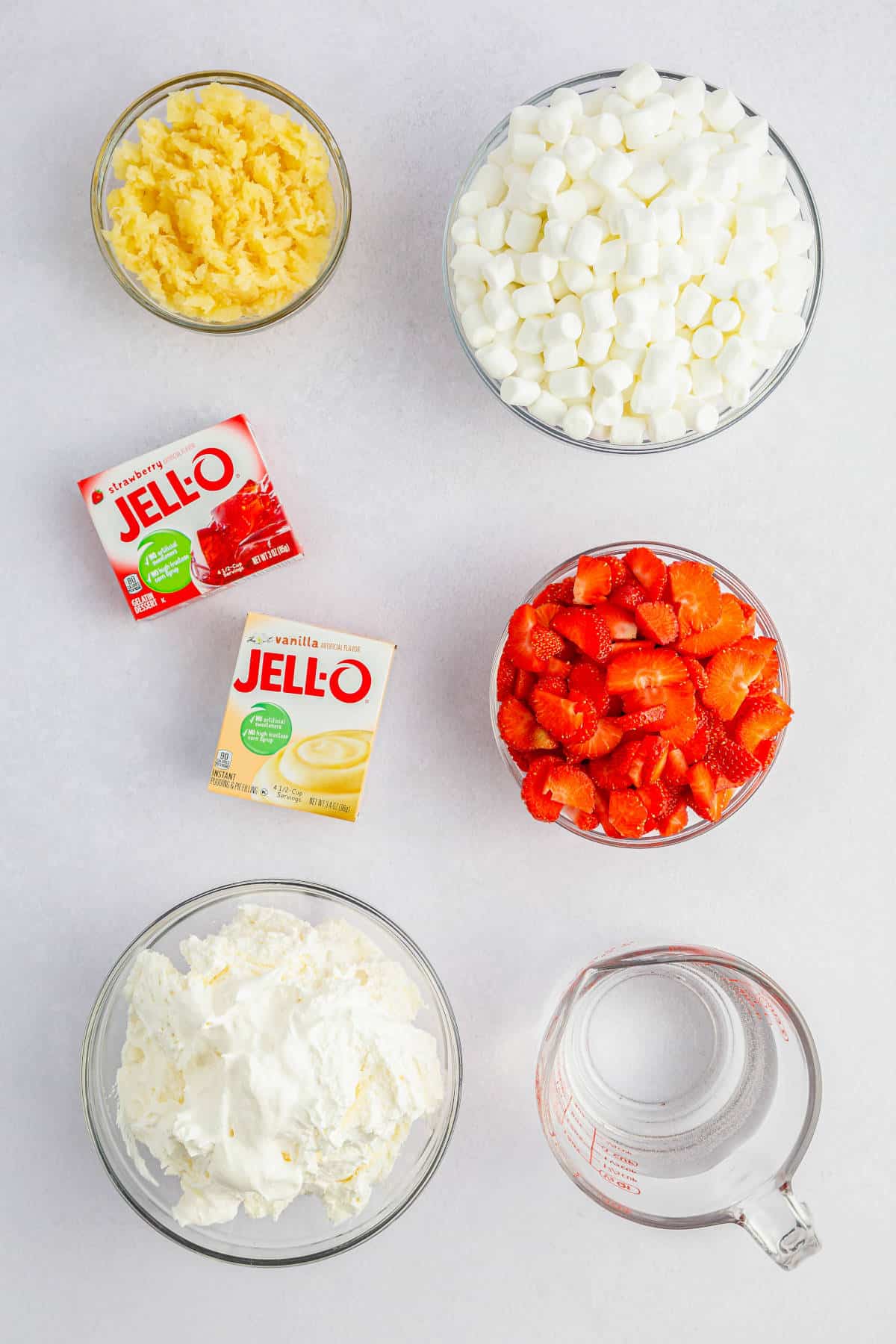 Ingredients for Strawberry Fluff Salad Recipe: strawberry jello mix, vanilla pudding mix, strawberries, pineapple, cool whip, marshmallows, and water.