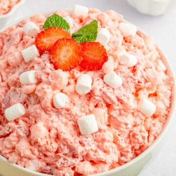 Strawberry jello salad in a white bowl topped with extra marshmallows.