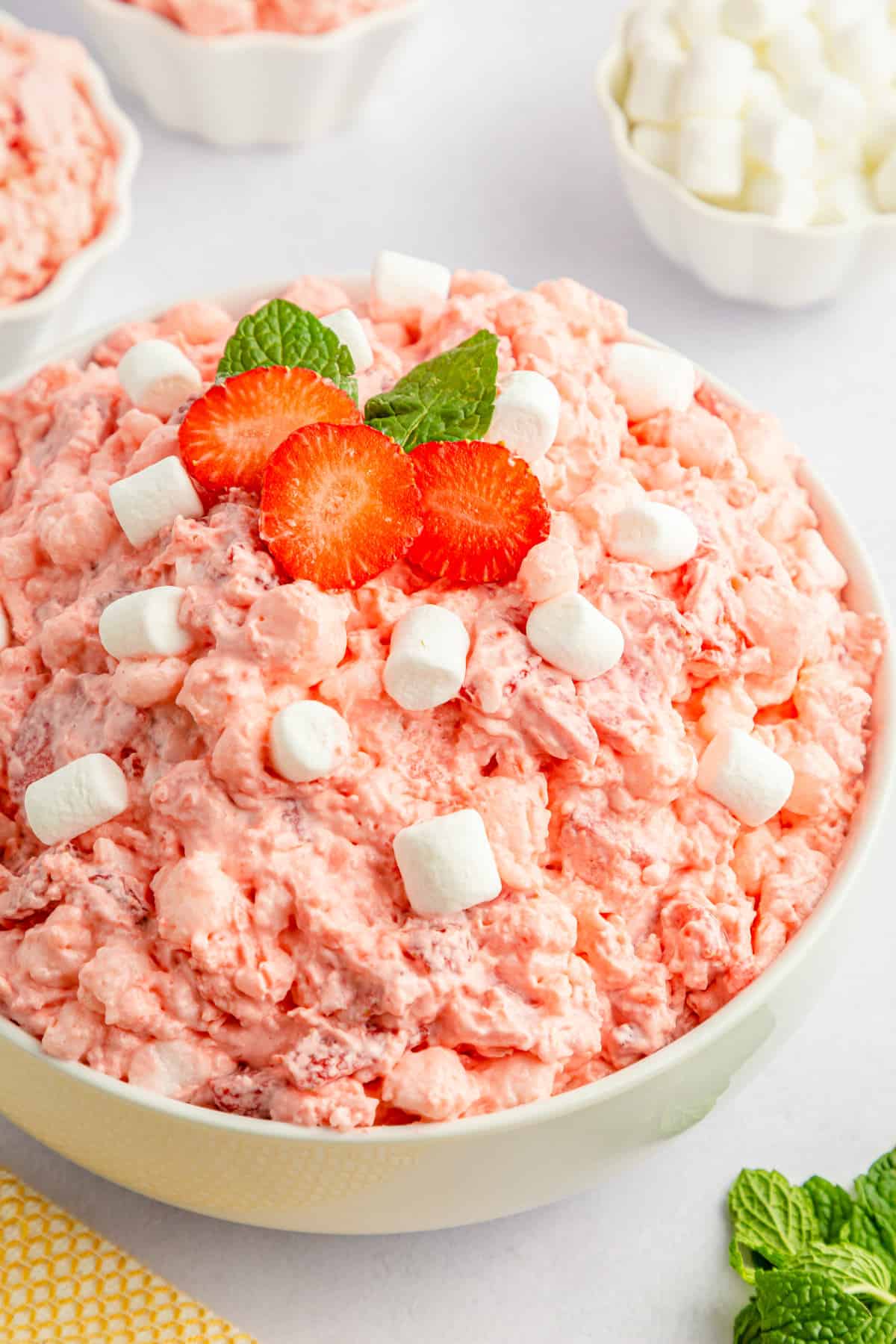 Strawberry jello salad in a white bowl and topped with extra marshmallows.