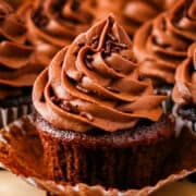 Moist chocolate cupcakes topped with chocolate frosting and sprinkles on a wooden table.