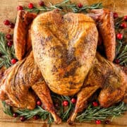 A smoked spatchcock turkey on a wooden cutting board decorated with cranberries and rosemary sprigs.
