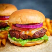 A pellet grill burger with tomato, onion, and lettuce on a sheet of brown parchment paper.