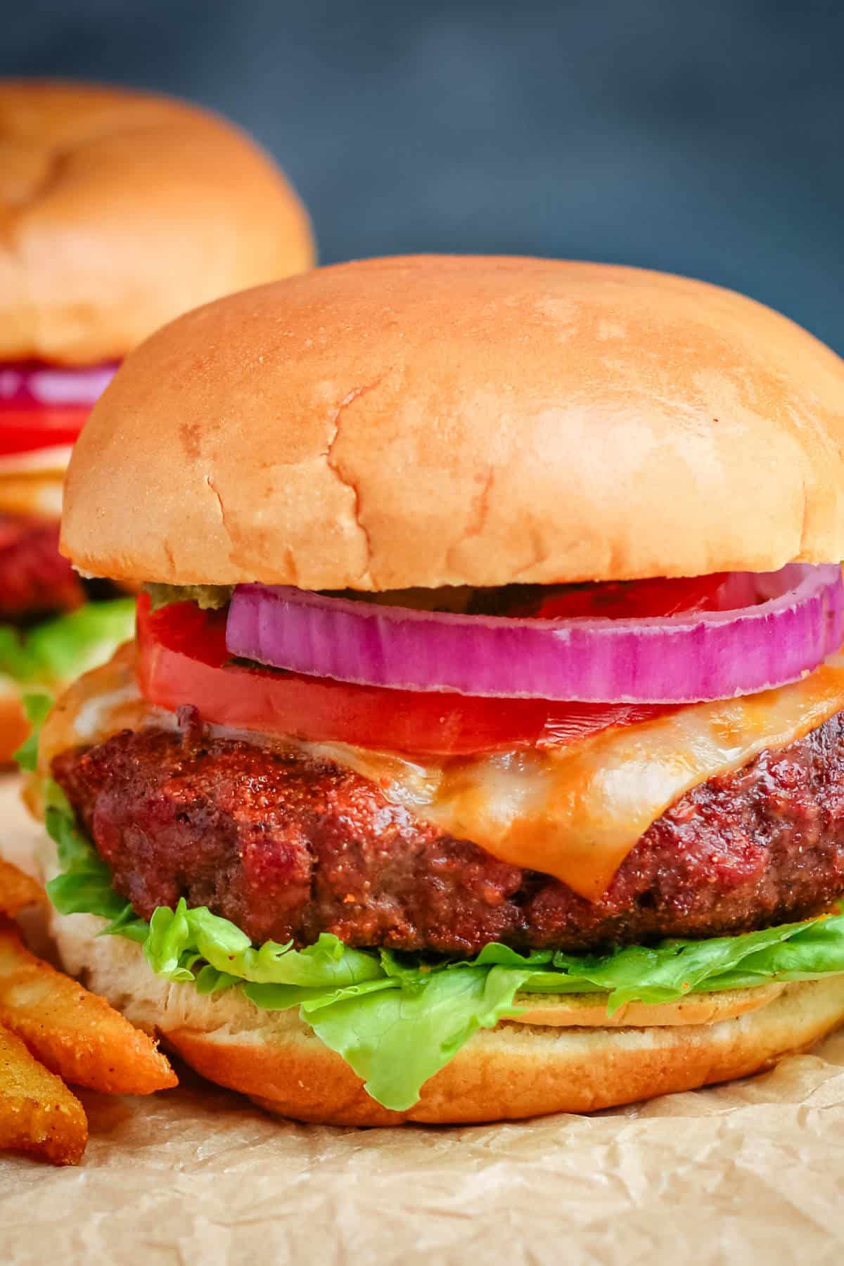 A pellet grill burger with tomato, onion, and lettuce on a sheet of brown parchment paper.
