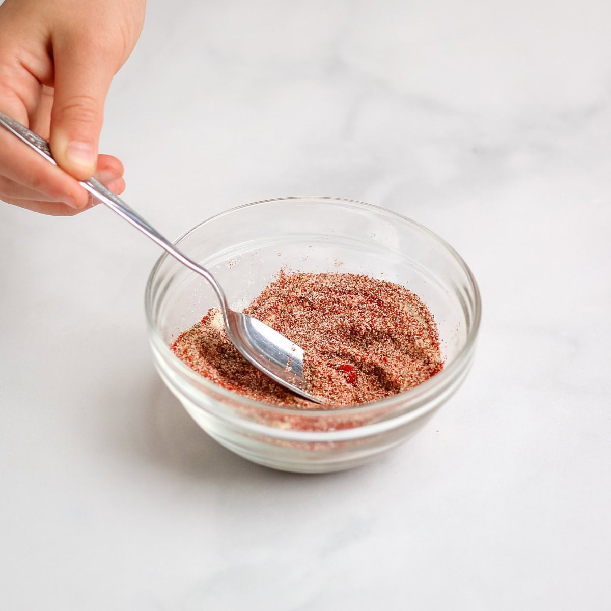 Stirring the burger seasonings together with a silver spoon in a small glass bowl.