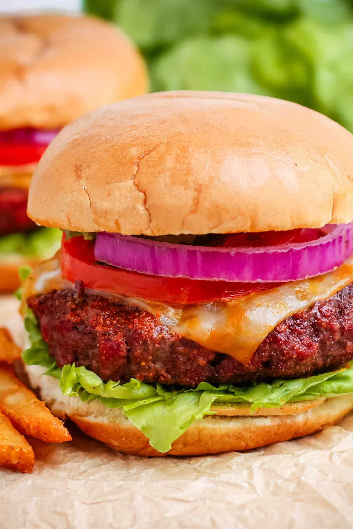 A close up of a pellet smoker burger with fries on a sheet of brown parchment paper.