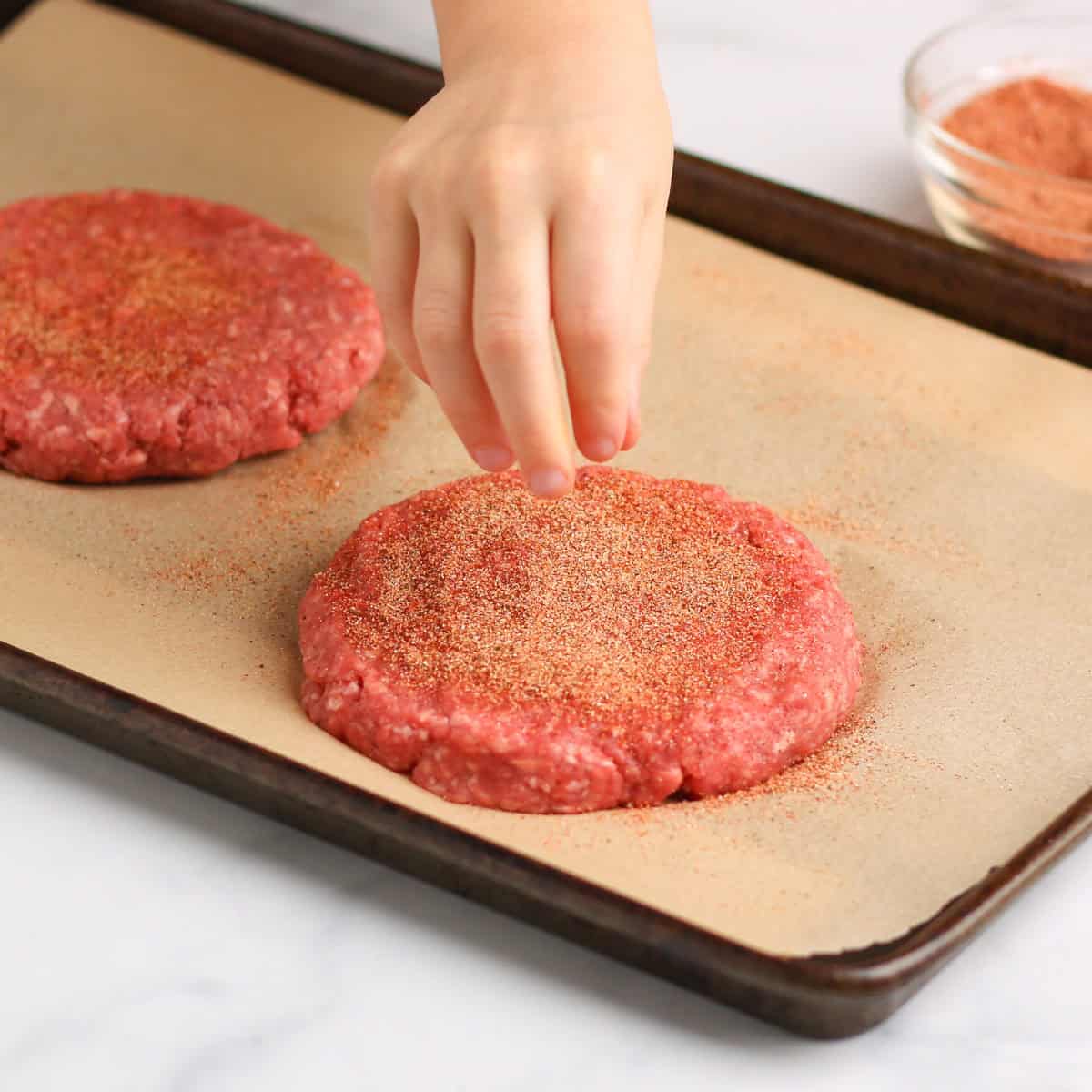 Seasoning the hamburger patties.