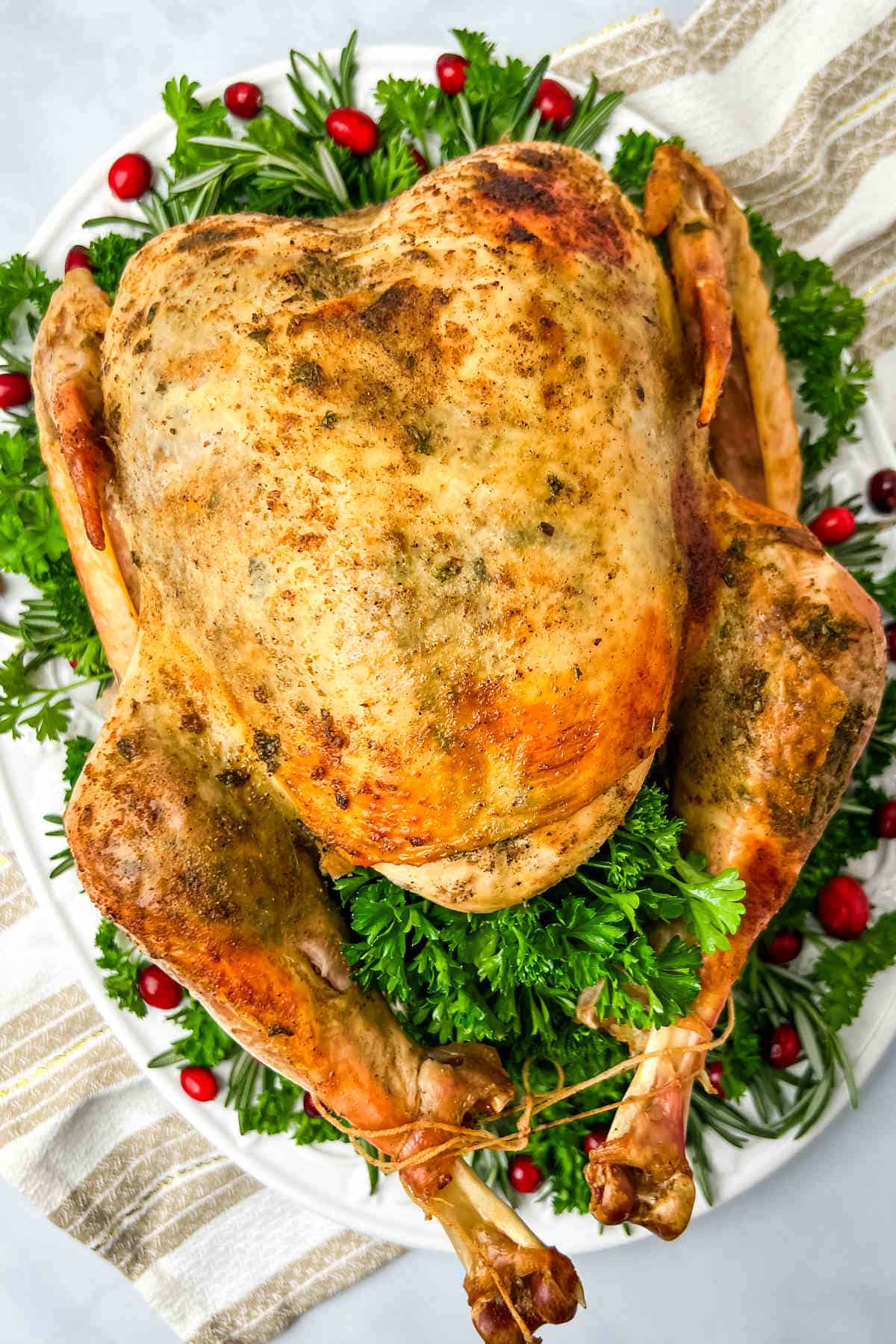 An overhead view of a whole turkey that has been baked in an oven bag on a white serving dish garnished with grape tomatoes and herbs.