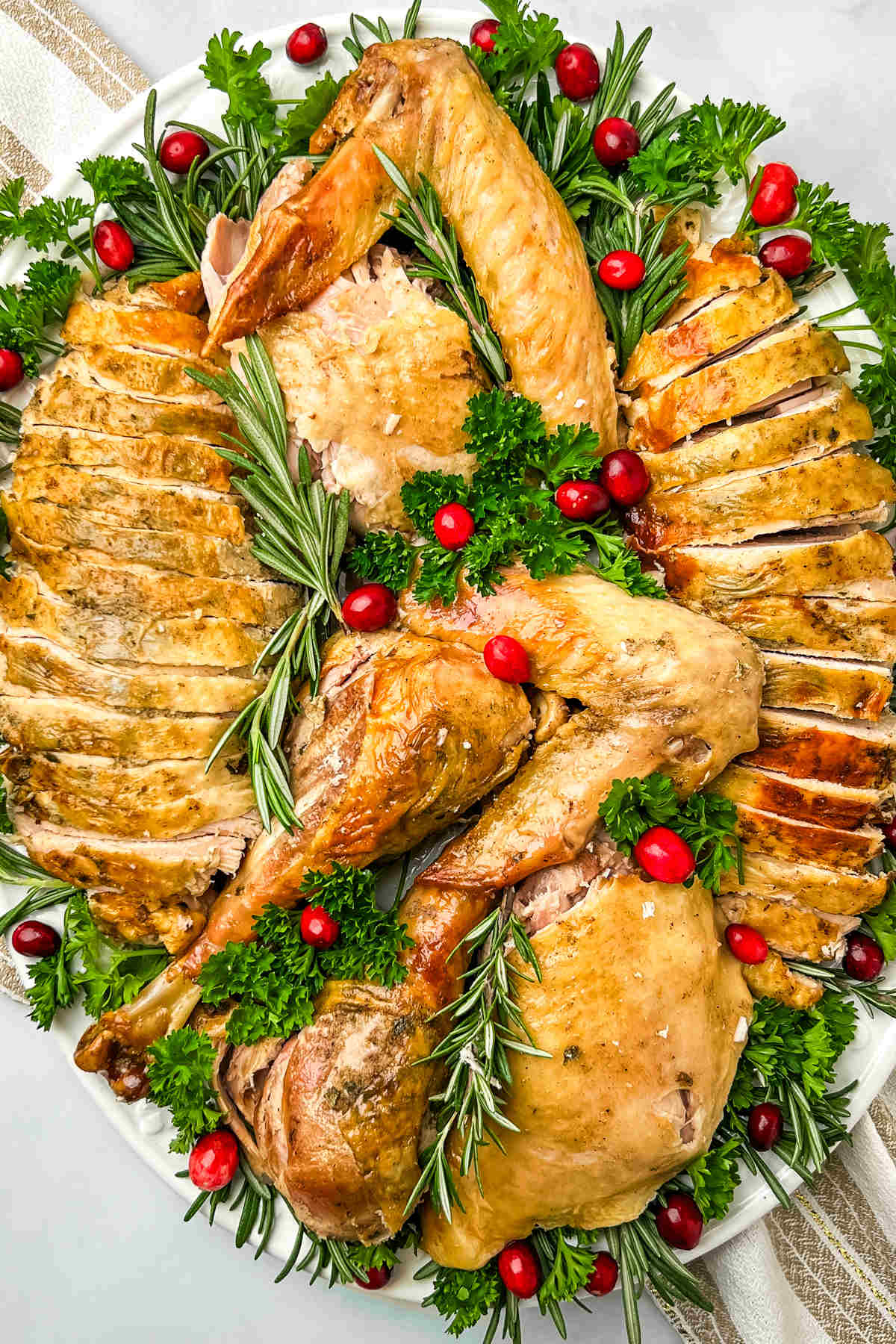 A carved turkey that's been baked in an oven bag arranged on a large serving platter and garnished with vegetables and herbs.